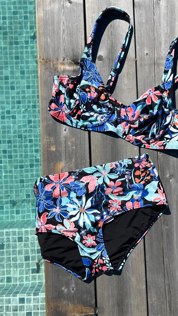 Blommig bikini mot en trätrall vid en kaklad pool